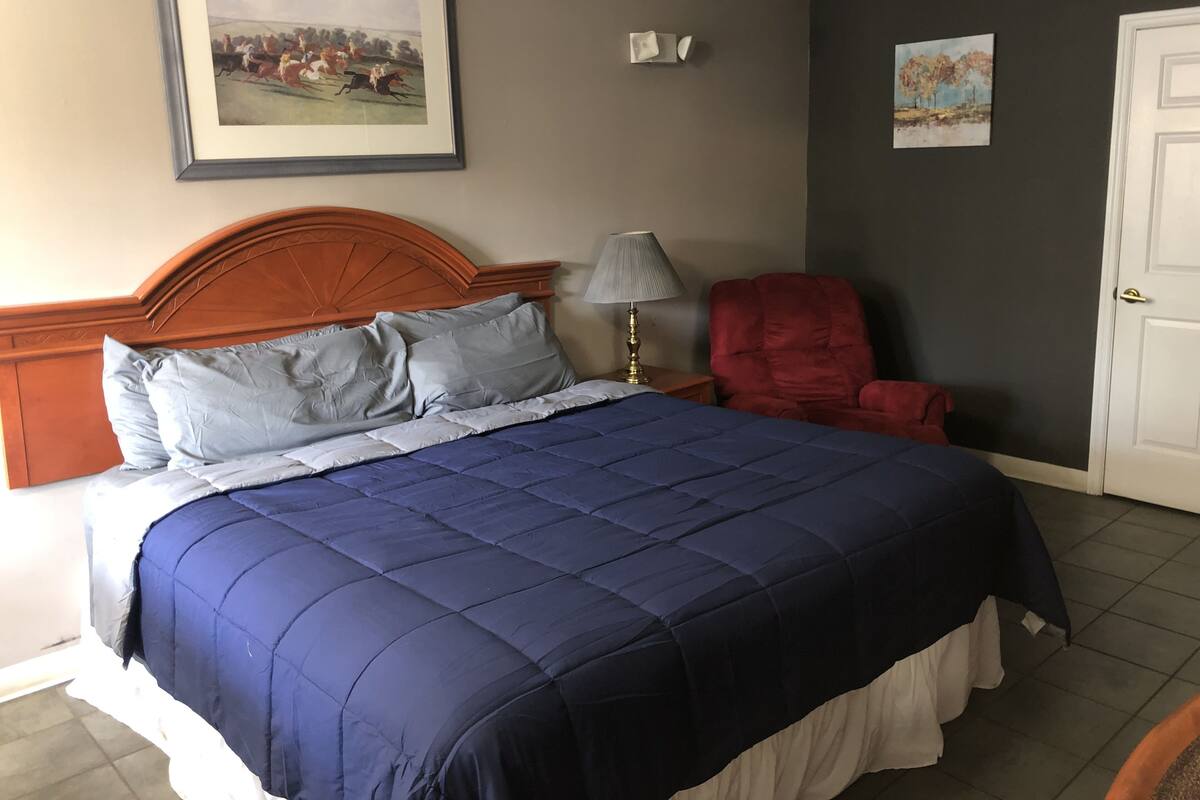 A bedroom with a large bed, a red chair, a lamp, and two framed pictures on the wall.