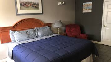 A bedroom with a large bed, a red chair, a lamp, and two framed pictures on the wall.