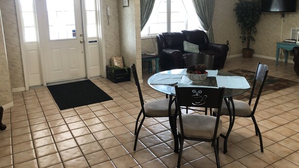 A dining area with a round table, four chairs, a chandelier, a black leather sofa, a television, and a potted plant. - The Tompkinsville Inn (Tompkinsville)