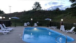 A swimming pool with lounge chairs and umbrellas, surrounded by a fence and a grassy hill. - The Tompkinsville Inn (Tompkinsville)