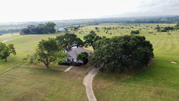 An aerial view of a rural property with a house surrounded by trees and open fields. - Spacious Country Living Located In The Heart Of Brenham (Brenham)