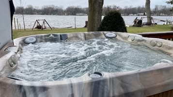 Relax in a hot tub with multiple jets on a spacious deck surrounded by a grassy lawn and a swing set.