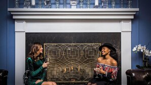 Two people seated on a bench in a room with a decorative fireplace, a patterned wall, and a vase of flowers. - The Read House Hotel Historic Inn and Suites (Chattanooga)