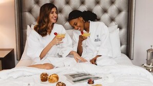 Two people in white robes sitting on a bed with a tufted headboard, holding drinks, and a breakfast spread including pastries and a newspaper. - The Read House Hotel Historic Inn and Suites (Chattanooga)