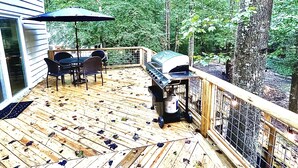 A wooden deck with a grill and dining area, surrounded by trees.