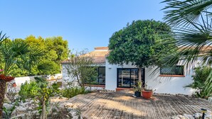 Una casa moderna con terraza de madera, rodeada de abundante vegetación y fachada blanca.