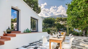 Un patio con suelo de baldosas, sillas blancas y una mesa de madera.