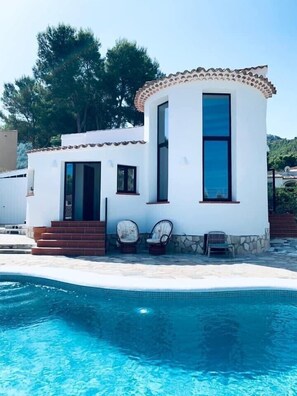 Un edificio blanco con tejado de baldosas y una piscina delantera.