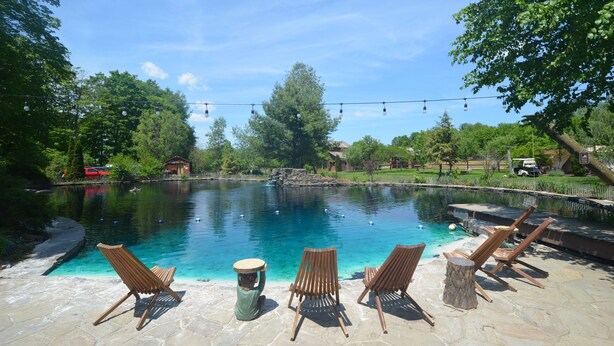 Une piscine à l’eau claire, entourée de carreaux de pierre et de chaises en bois.
