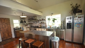 Une cuisine avec un îlot central, des tabourets de bar, des appareils en acier inoxydable et une poubelle.