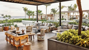 A covered outdoor lounge area with seating, a pool, and palm trees. - Etéreo, Auberge Collection (Playa del Carmen)