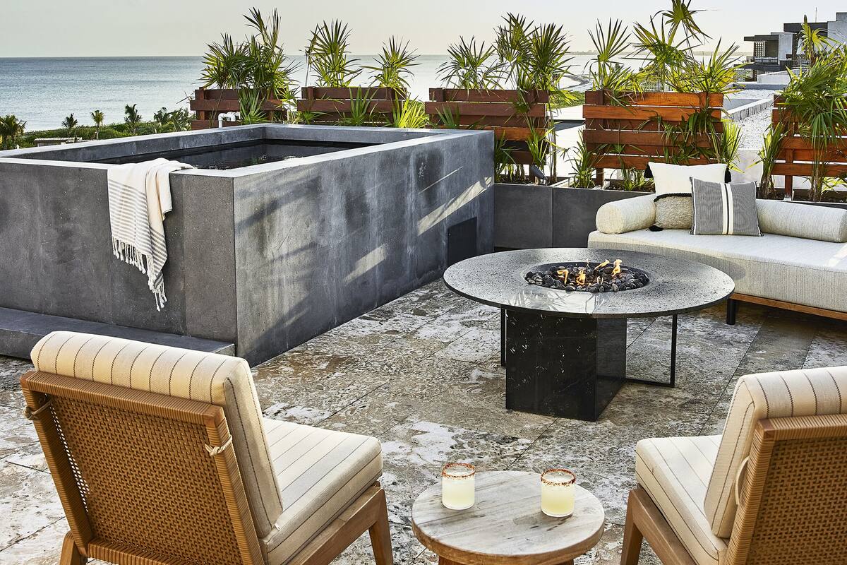 A rooftop terrace with seating, a fire pit, and a view of the ocean.