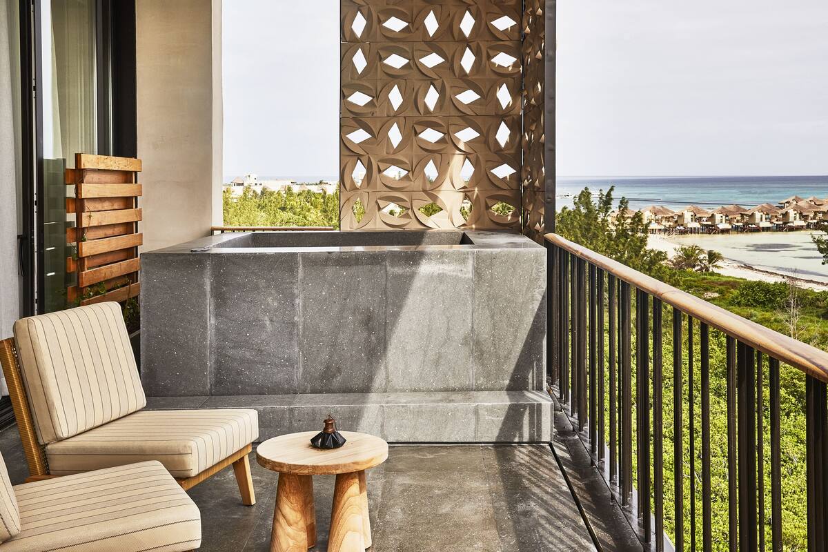 A balcony with a stone bench, a wooden chair, and a small round table with a decorative item.