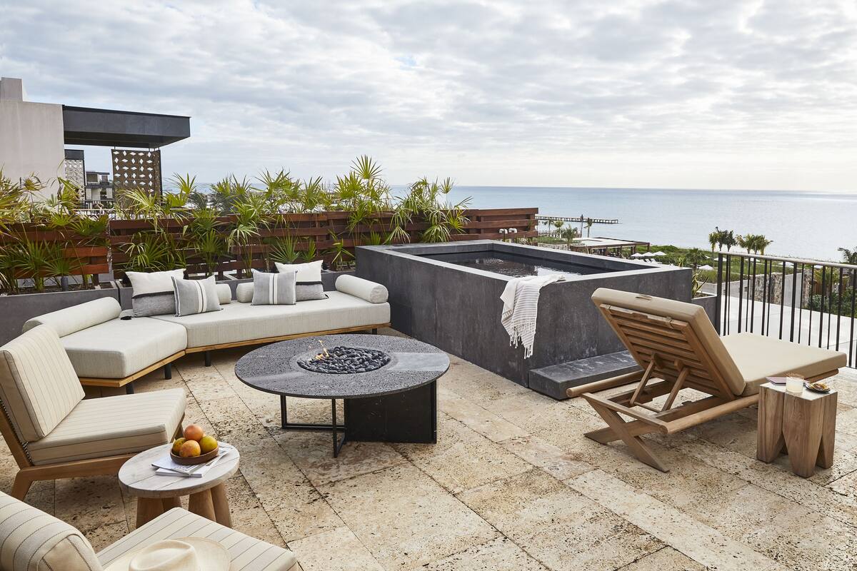 A rooftop terrace with a curved sofa, a round table with a fire pit, and a lounge chair.