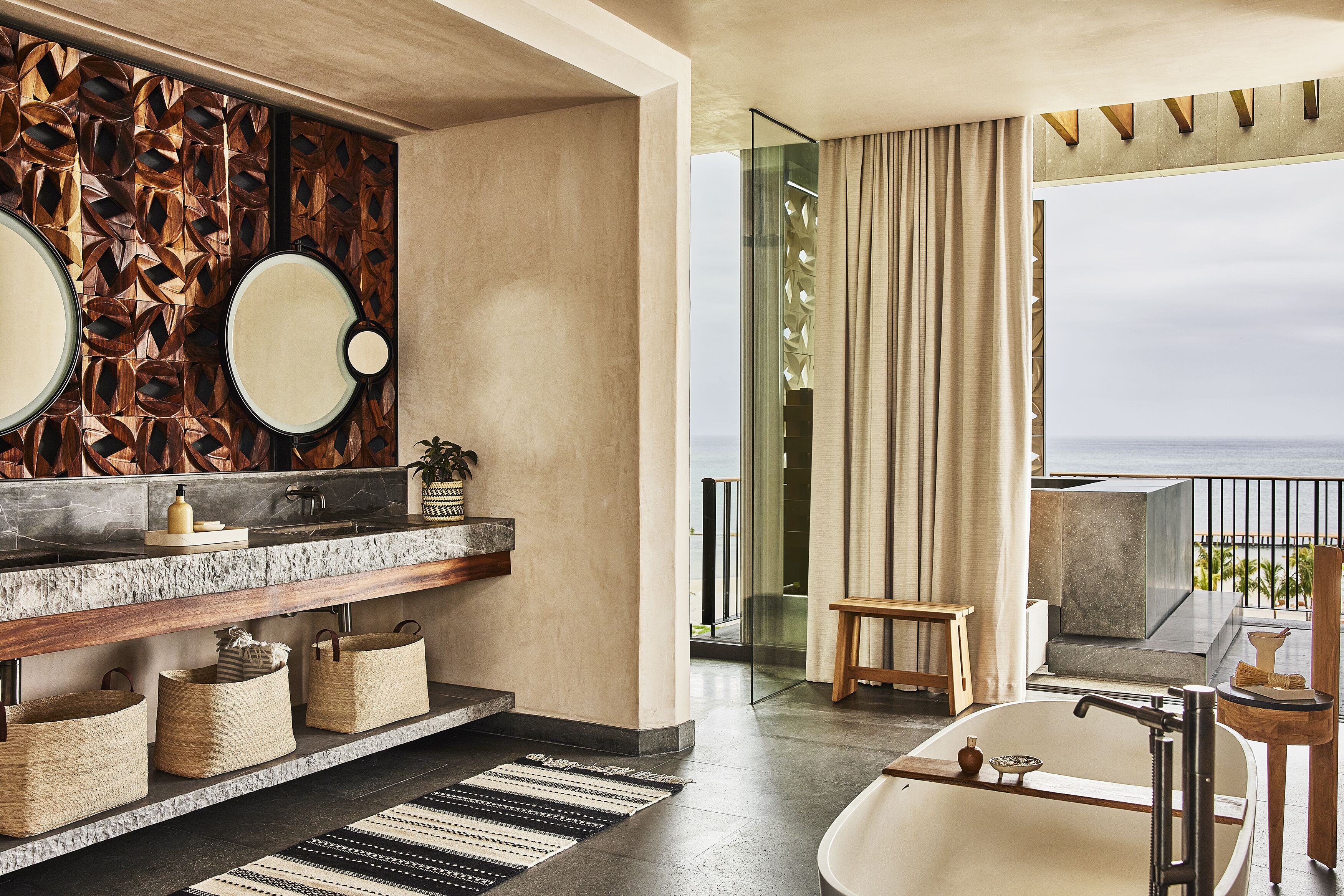 A modern bathroom with a large bathtub, a vanity with a mirror, and a view of the ocean.