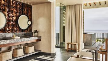 A modern bathroom with a large bathtub, a vanity with a mirror, and a view of the ocean.
