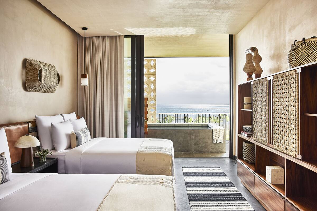 A hotel room with two beds, a balcony with a view, and a wooden wardrobe.
