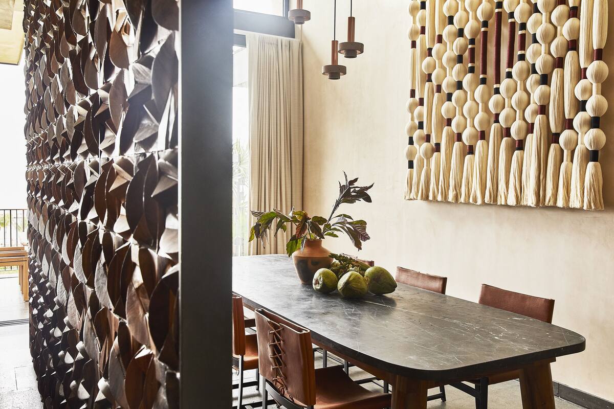 A dining area with a wooden table, chairs, a potted plant, and a decorative wall with geometric patterns.