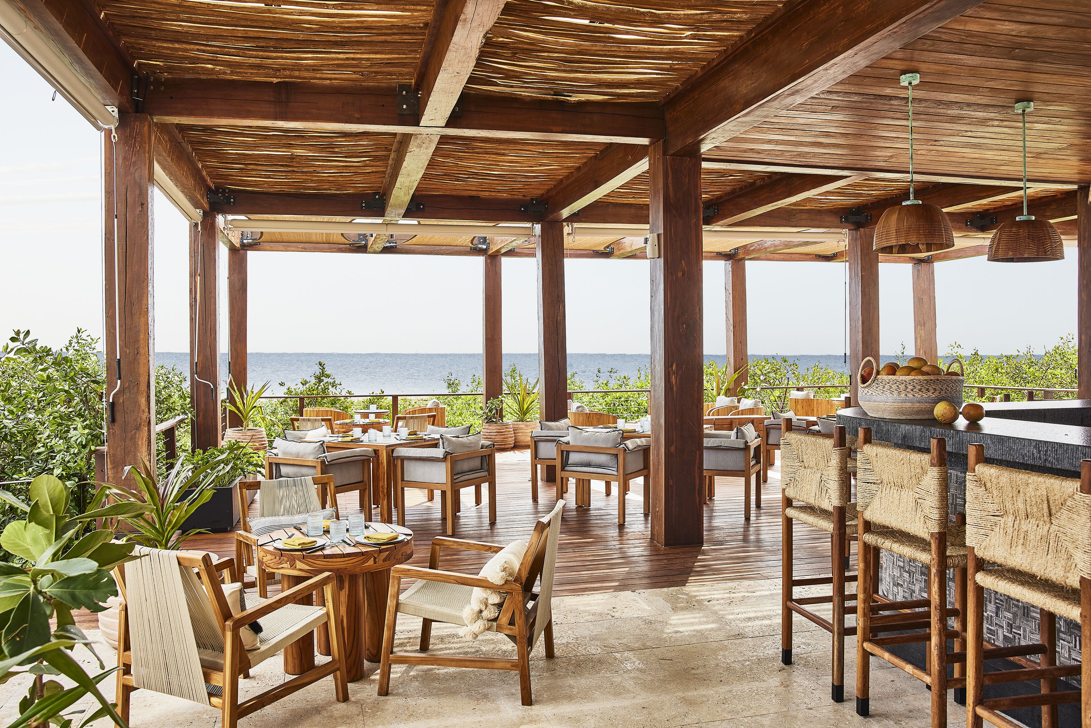 Un espacio de patio al aire libre con mobiliario de madera, un bar y vista al mar.