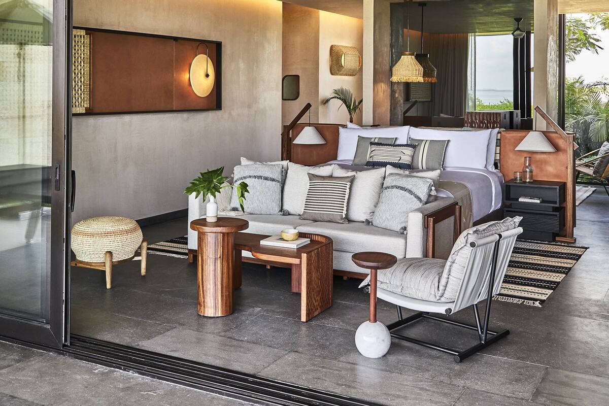 A modern bedroom with a large bed, a sofa, and a coffee table. There is a window with a view of the ocean.