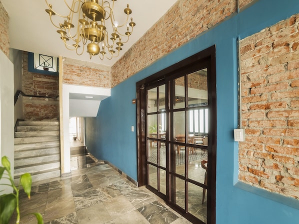 A hallway with a staircase, a blue wall, a brick wall, and a chandelier.