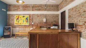 A reception area with a wooden desk, a computer, a ceiling fan, and a brick wall.