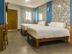A hotel room with two single beds, a wooden desk, a chair, a window with curtains, and patterned tile walls.