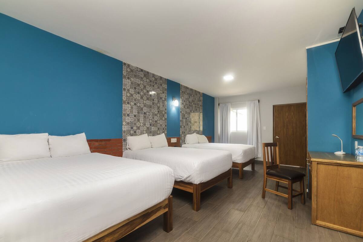A hotel room with two beds, a wooden desk, a chair, and a mirror.