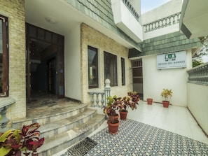 A hotel entrance with a tiled patio, potted plants, and a sign for 'Meson Del Barrio Hotel'.