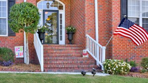 A brick building with a white front door, a small porch, and an American flag. - Master's Rental (Evans)