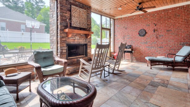 A covered patio with wicker furniture, a stone fireplace, and a dartboard. - Master's Rental (Evans)