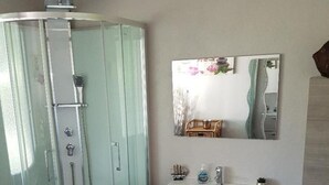 A bathroom with a glass-enclosed shower, a white sink with a mirror above it, and a beige rug on the floor. - Charming little house "LA BIKOK (BILLY)