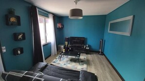 A room with teal walls, a black sofa, a television, and a ceiling light. - Charming little house "LA BIKOK (BILLY)