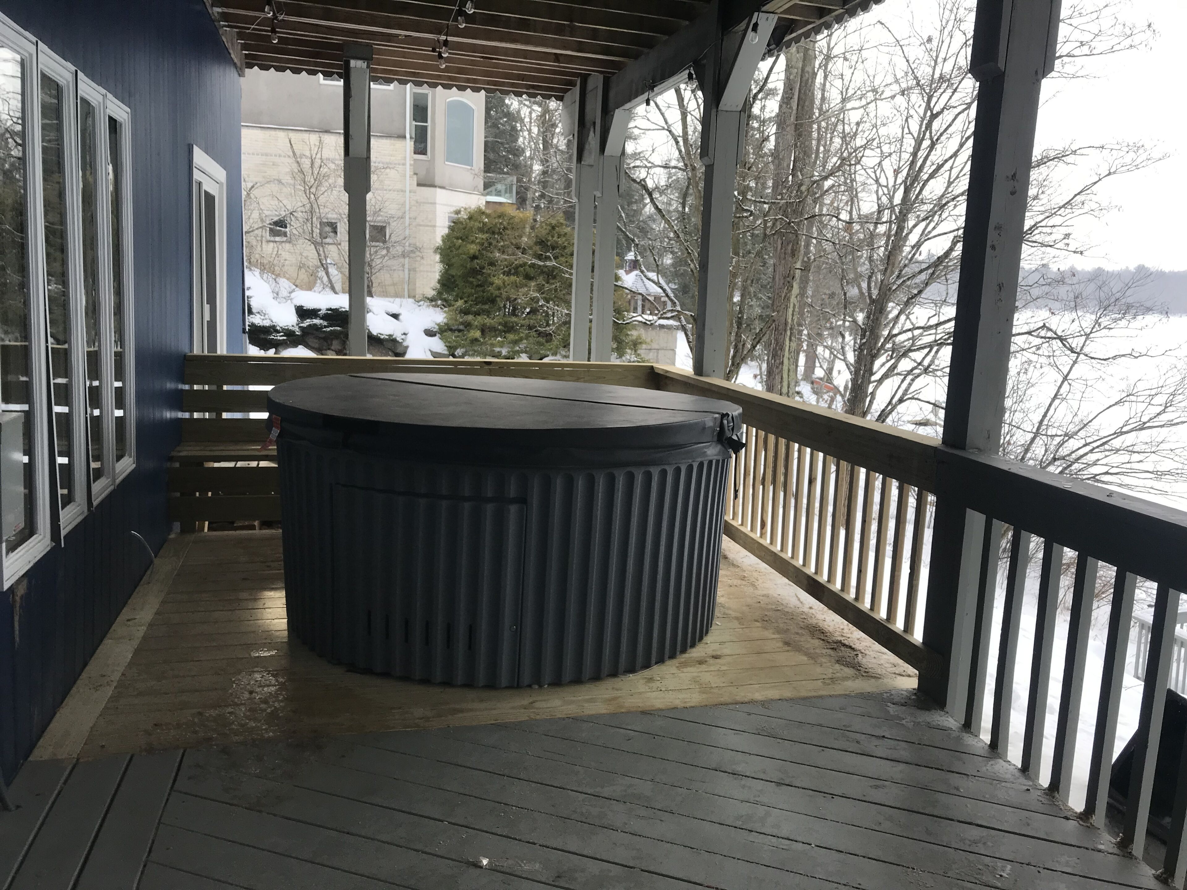 A covered outdoor area with a hot tub, wooden deck, and a view of a snowy landscape.