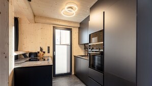 Moderni keittiö, jossa on suuri keittiösaareke, integroidut kodinkoneet ja liukuovi parvekkeelle.