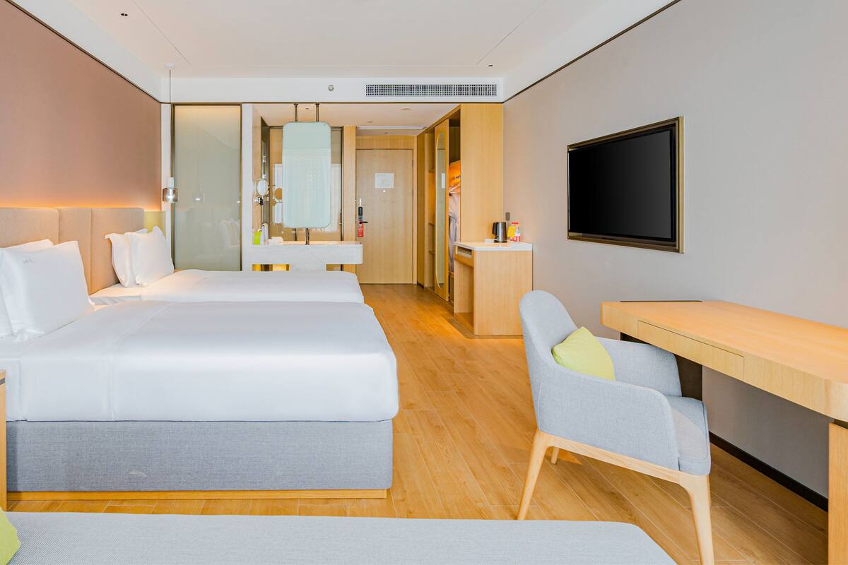 A hotel room with a large bed, a desk, a chair, a TV, and a bathroom visible through an open door.