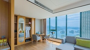 A modern hotel room with a large window, a cozy seating area, a vanity with a mirror, and a wardrobe. - Holiday Inn One Thousand Island Lake by IHG (Hangzhou)