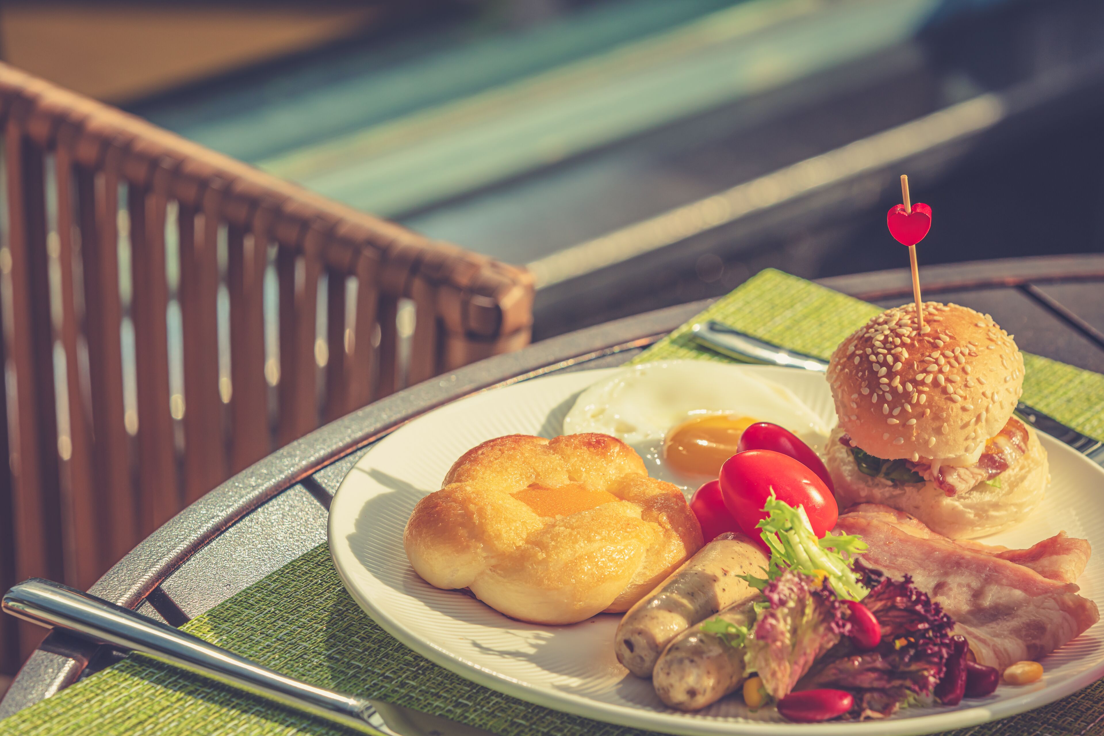 Un plato con alimentos de desayuno como huevos, salchicha, tocino y una hamburguesa, sobre una mesa con una servilleta verde.