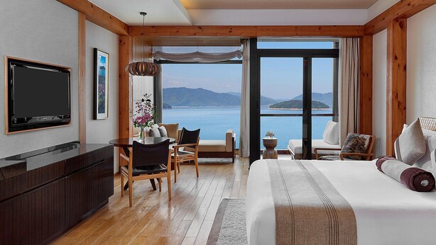 A hotel room with a large bed, a TV, a dining area, and a view of the sea. - Holiday Inn One Thousand Island Lake by IHG (Hangzhou)