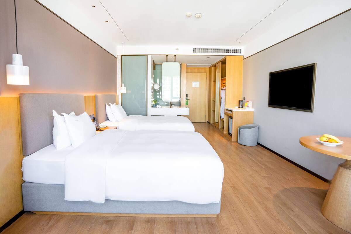 A modern hotel room with a large bed, a TV, and a small table with a fruit bowl.