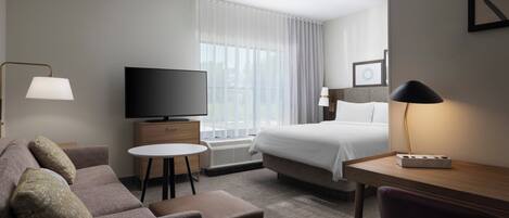 A hotel room with a bed, a TV, a desk, a chair, a sofa, and a small table.