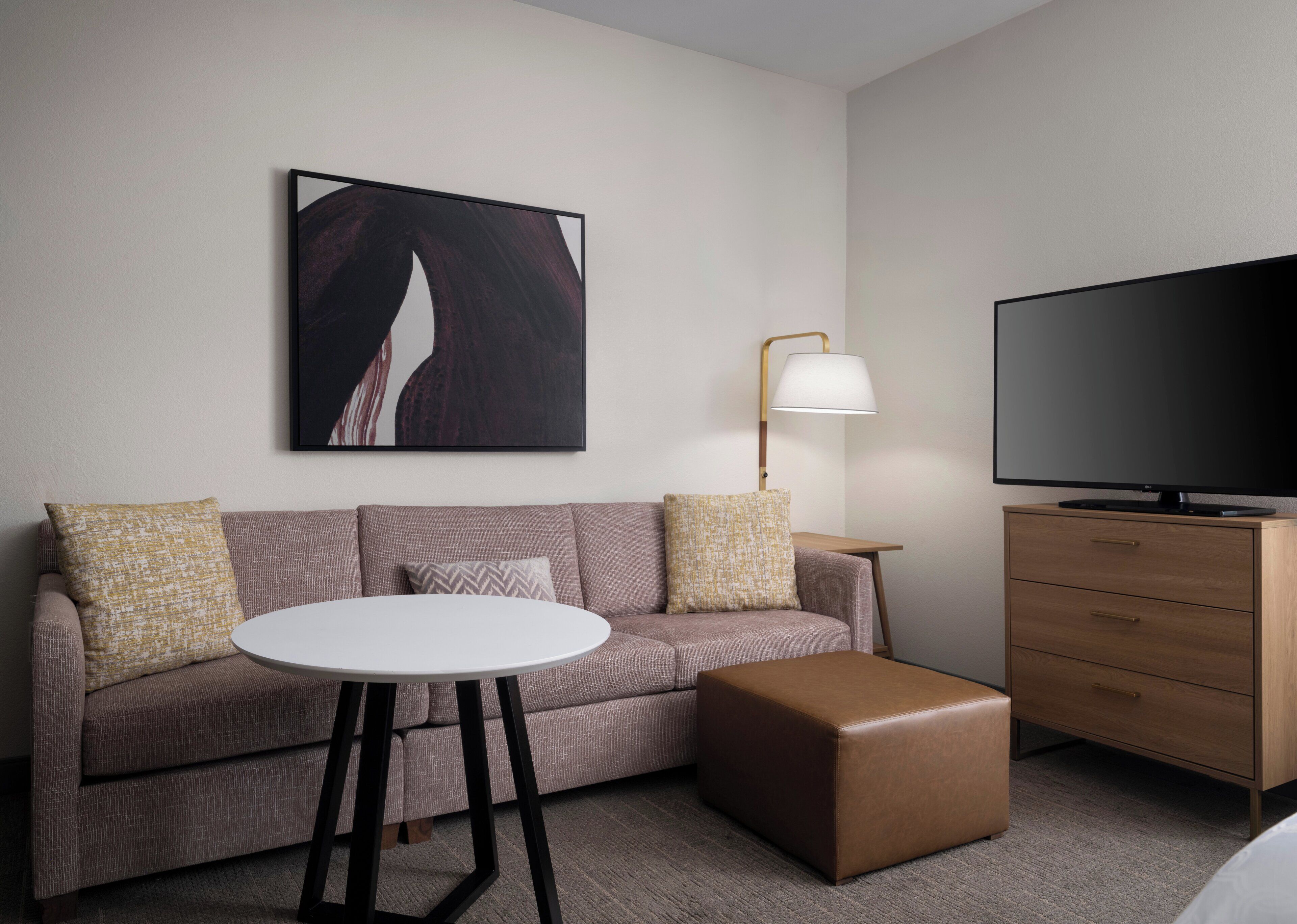 A modern hotel room with a sofa, a small round table, a television, and a lamp.