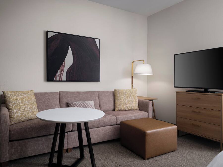 A modern hotel room with a sofa, a small round table, a television, and a lamp.