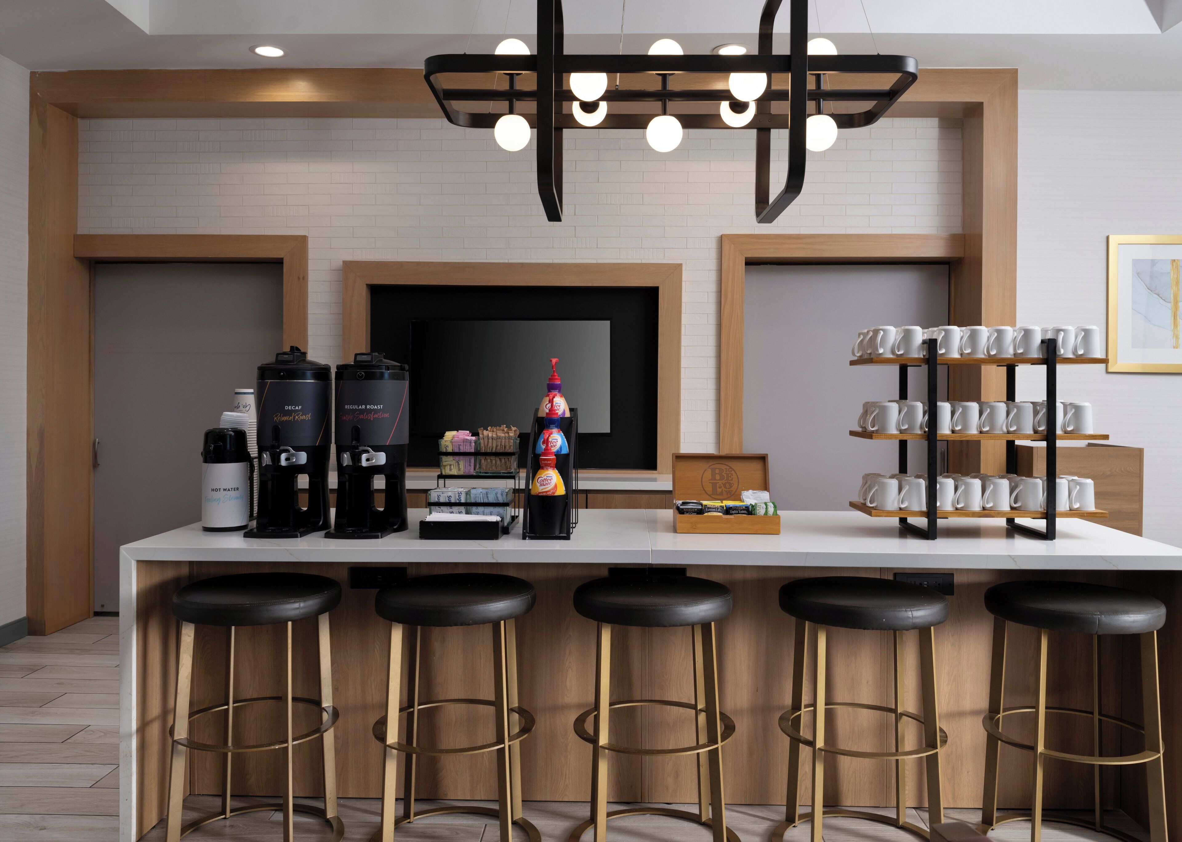 A modern kitchen with a bar area, equipped with coffee machines, a coffee station, and a mug display.