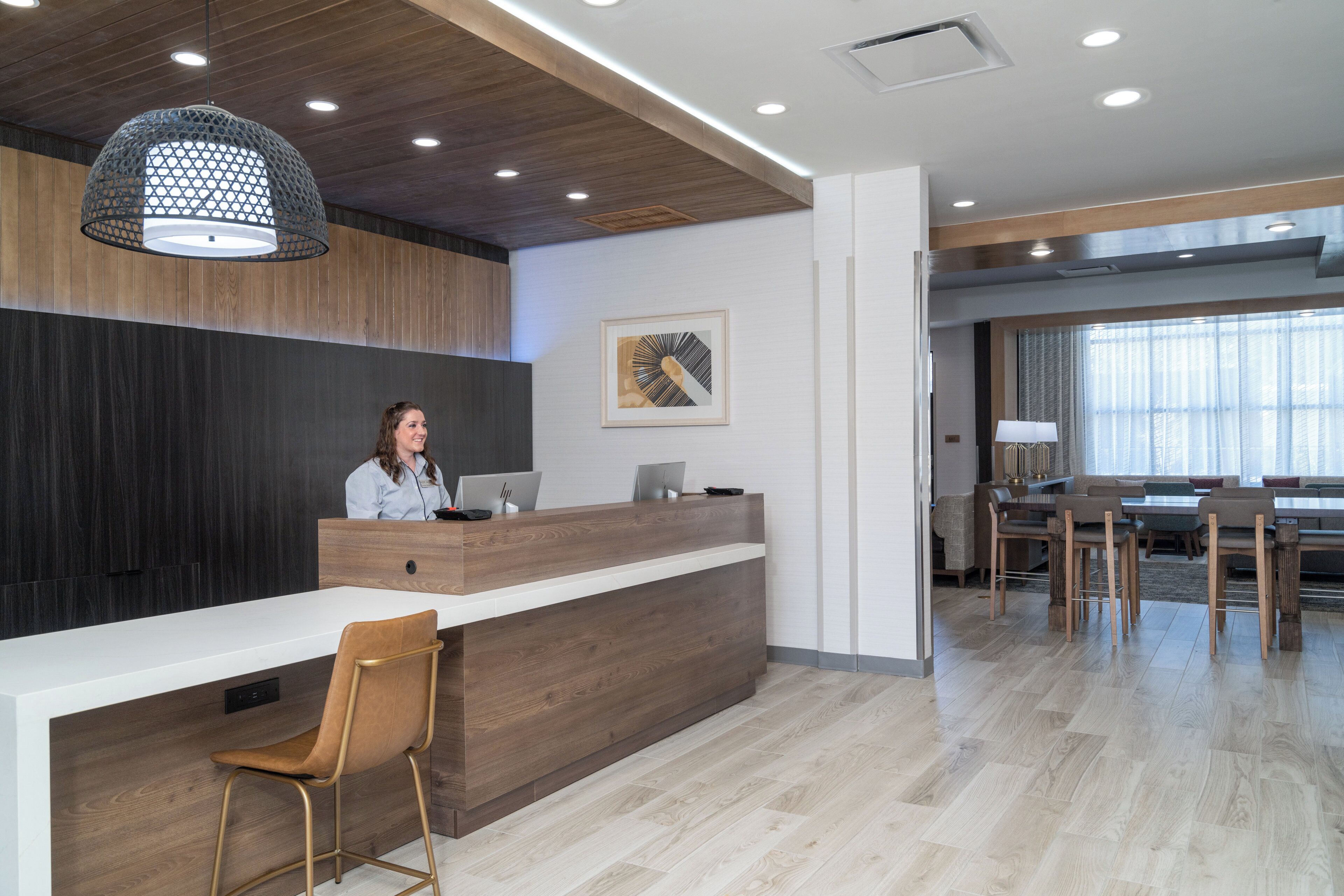 A reception desk with a wooden counter, a single chair, and a person seated behind it.