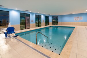 Piscina interior con señalización de seguridad visible, una silla azul y un asiento para socorristas.