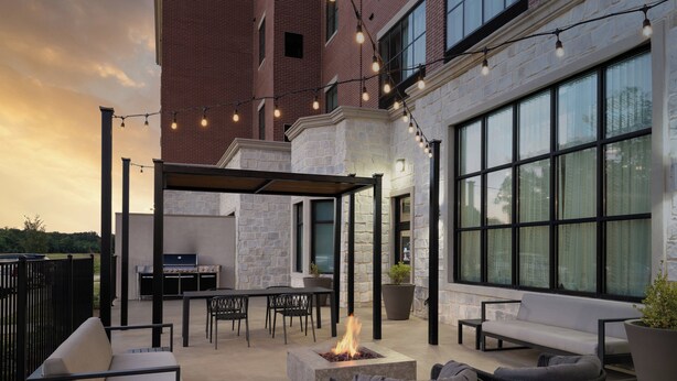 An outdoor patio with stone walls, a grill, seating, and string lights. - Staybridge Suites Flowood Nw Jackson by IHG (Flowood)