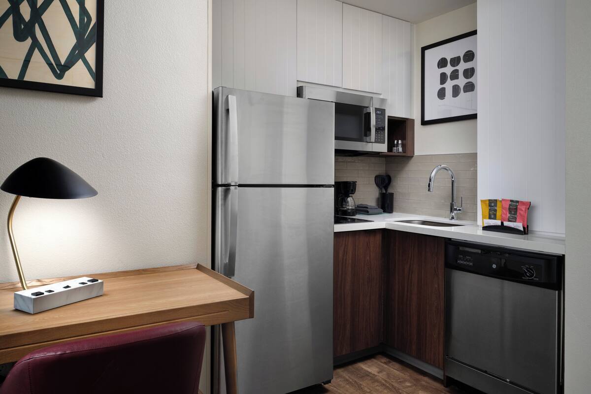 A modern kitchen with stainless steel appliances, a wooden dining table, and a red chair.