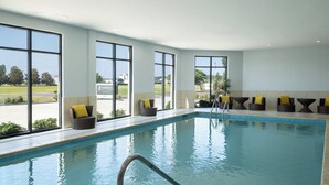 A swimming pool with a clear view of the outside, large windows, and several wicker chairs with yellow cushions. - Staybridge Suites Flowood Nw Jackson by IHG (Flowood)