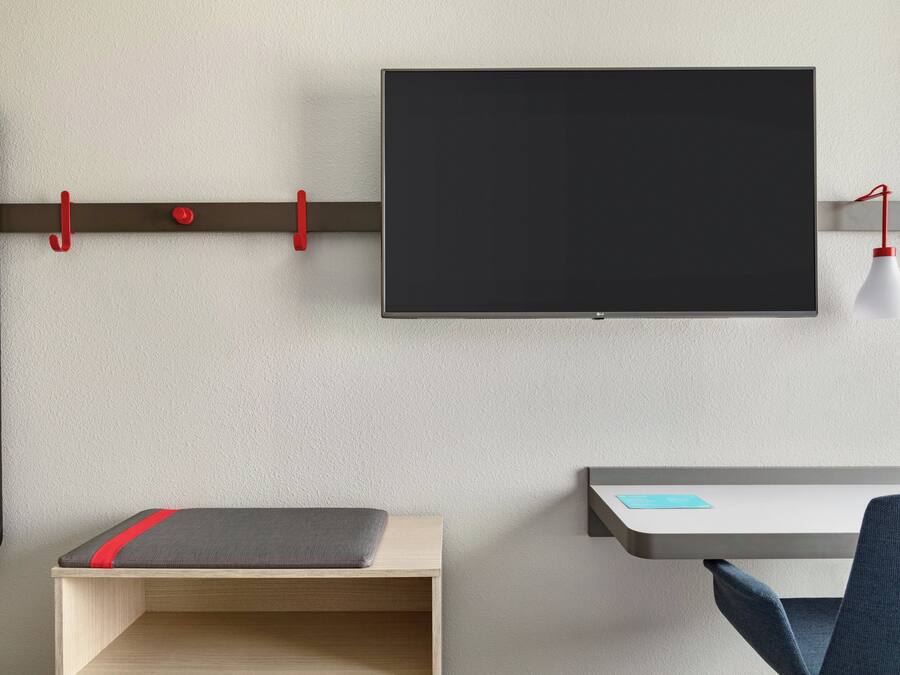 Una habitación moderna con una televisión de pantalla plana en la pared, un escritorio con una silla y un banco con una banda roja.